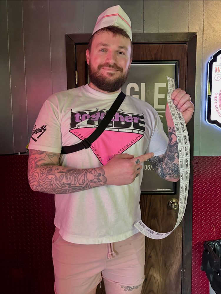 Chris wearing a paper butcher’s hat and holding a string of raffle tickets