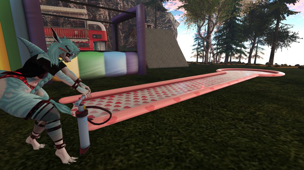 Skye, a humanoid shark, uses an air pump to inflate a slip-n-slide in a grassy field. There is a rainbow bounce house and trees in the background.