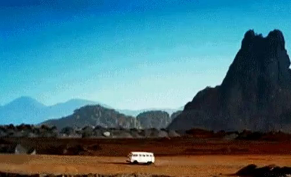 a white van is driving through a deserted area with mountains in the background