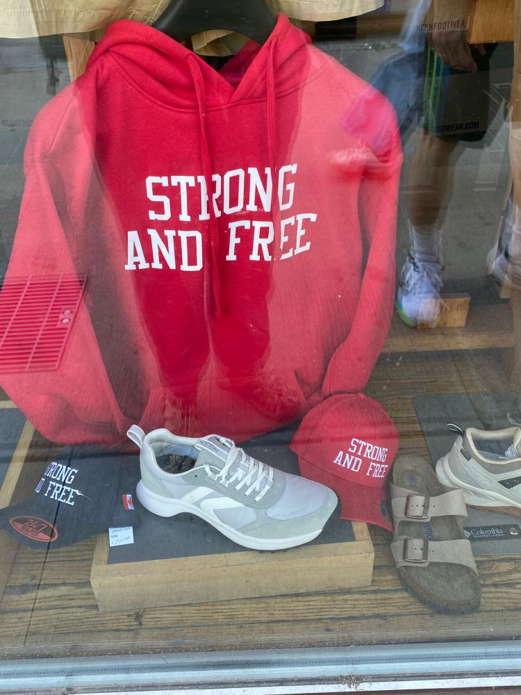 Shop window showing a bright red hoodie and two baseball hats, one red and one black, with the words "STRONG AND FREE" on them.