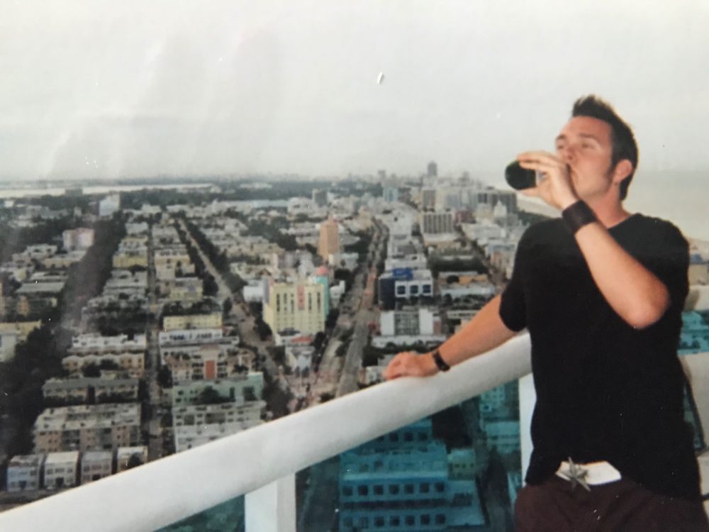 punk rocker drinking a beer near the railing of a rooftop overlooking a city
