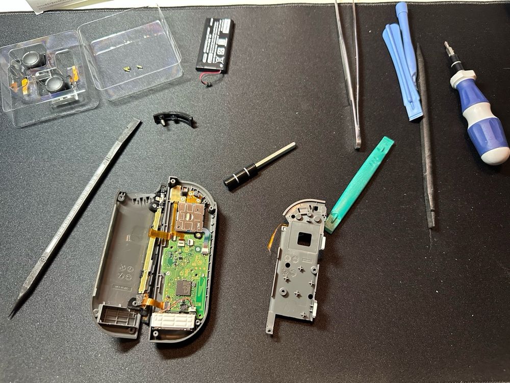 A game controller partially disassembled and scattered on a black mat along with an assortment of small tools. 