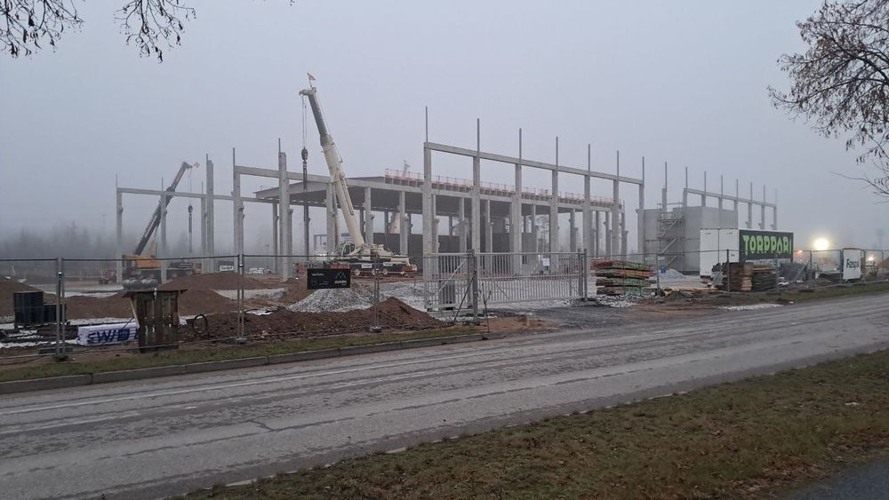 Construction yard for a huge hall supported by concrete beams with a few cranes setup. It is very foggy outside.