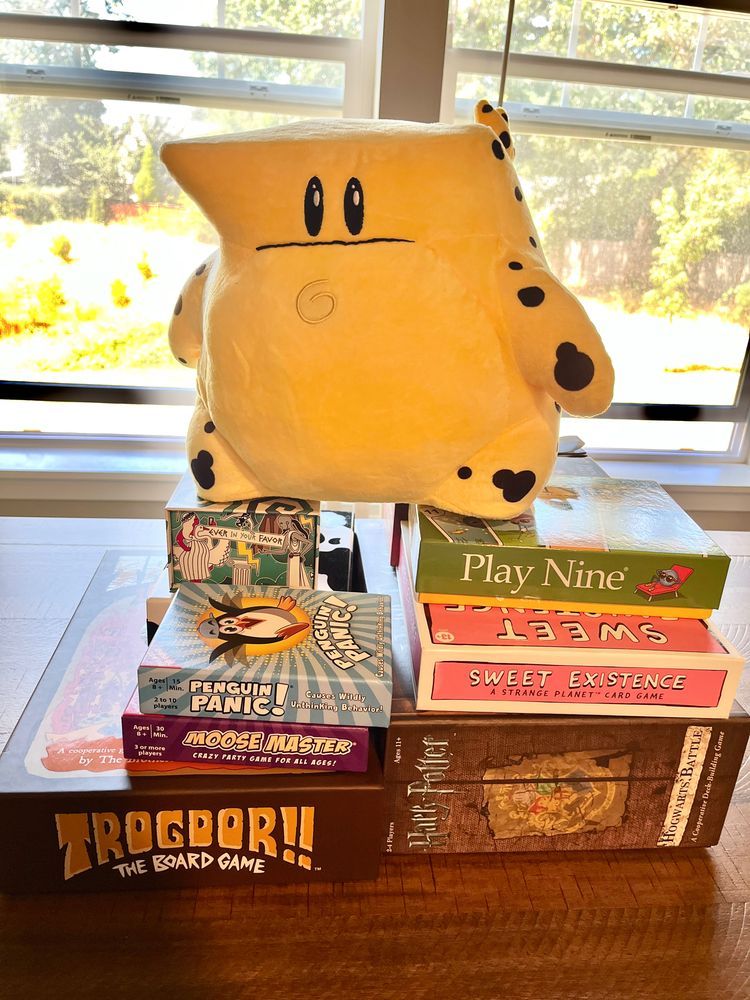 Kick the Cheat! plushie on top of a pile of board games (including TROGDOR: The Game)