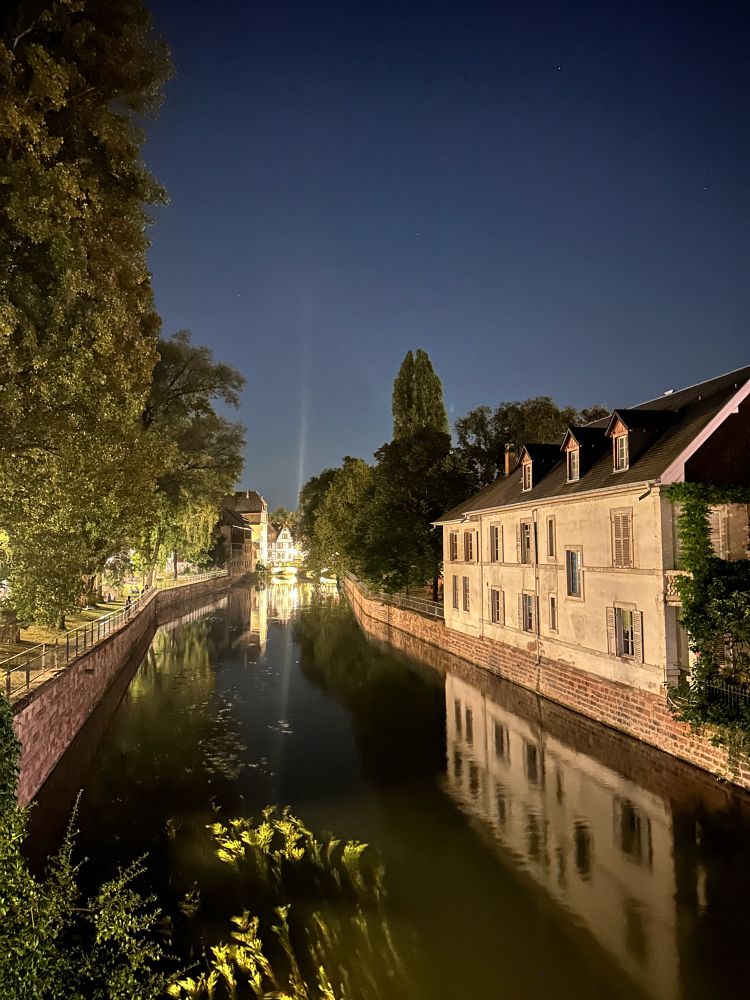 Ein weiteres Bild mit Blick auf einen Kanal in Straßburg bei Nacht. Der Kanal ist von Fachwerkhäusern gesäumt, die Häuser auf dem Bild sind angestrahlt.