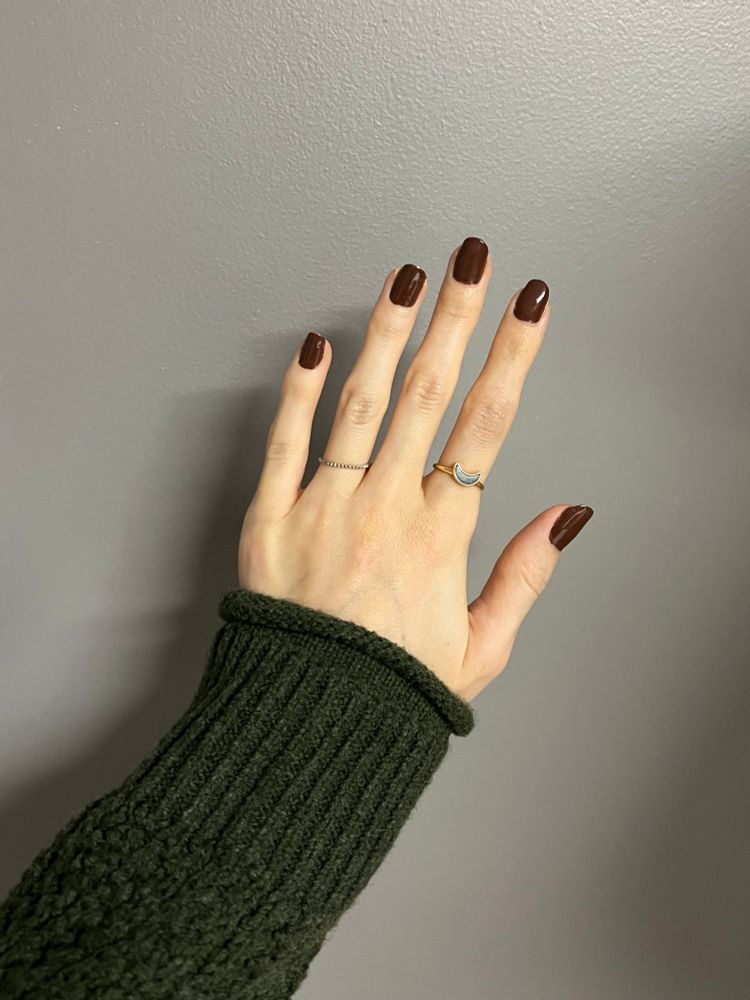 my hand against a grey wall. my nails are painted a dark chocolate color