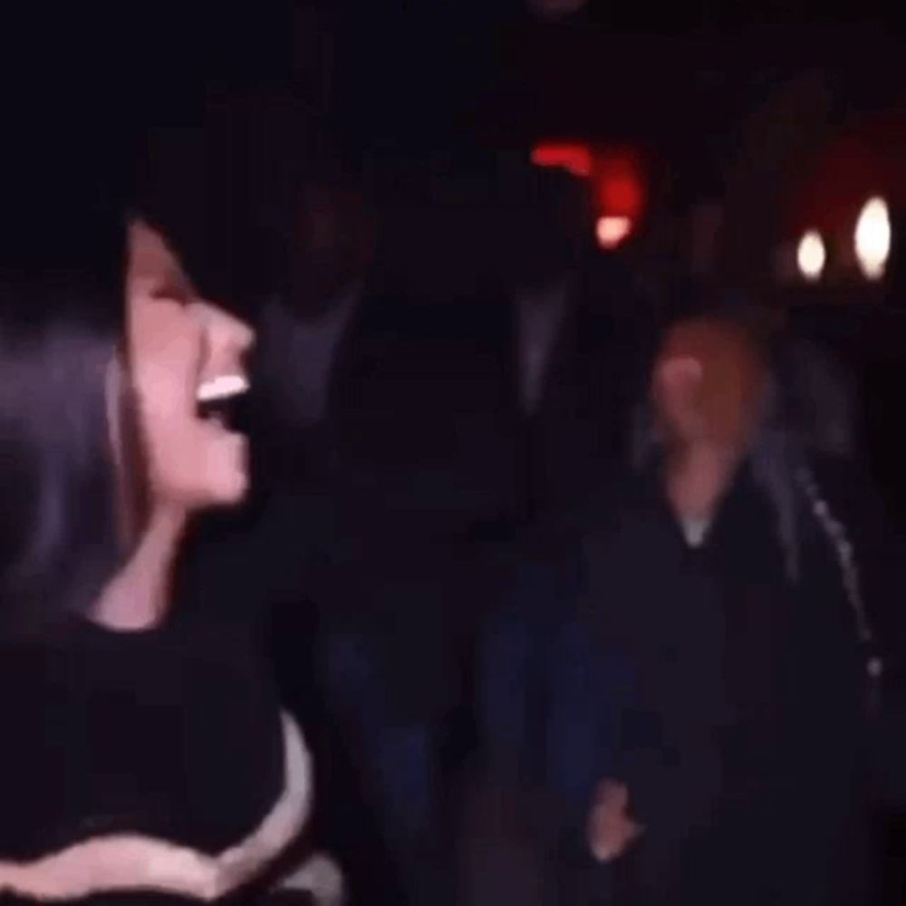 a woman is laughing and dancing in a dark room with a crowd behind her .