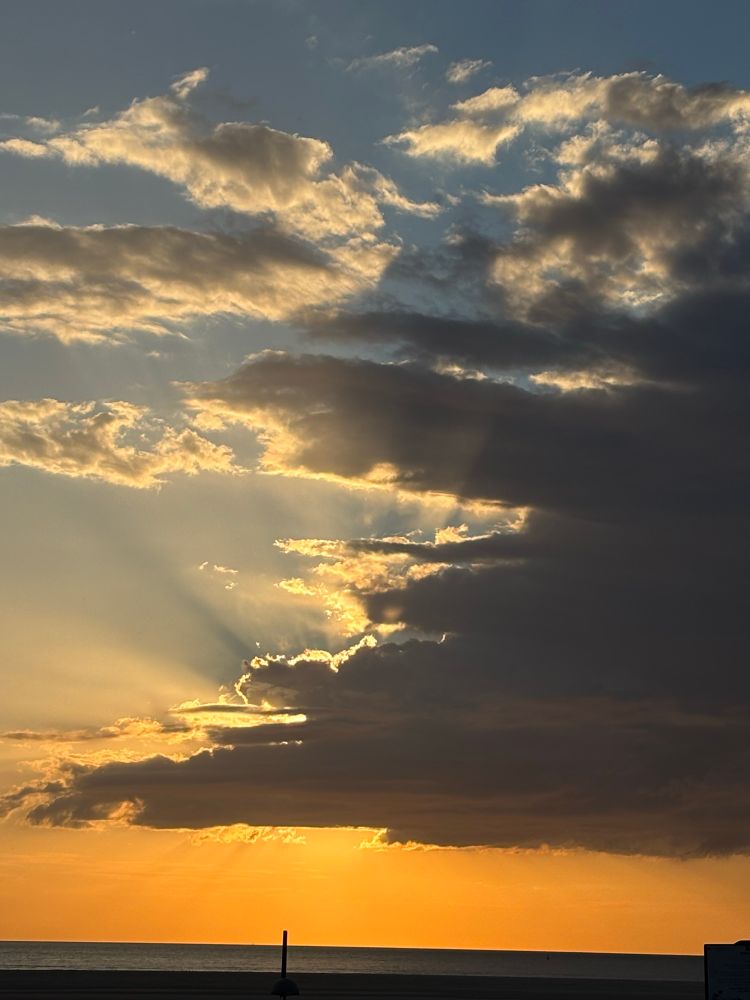 Abendsonne hinter Wolken, Hintergrund rötlich gefärbt.