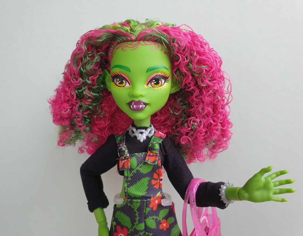 Doll photo. Monster High Fearbook Venus McFlytrap with green skin, coiled pink and green hair, wearing black, green and red floral overalls over a black long-sleeve crop top and thorny silver choker and bracelet.