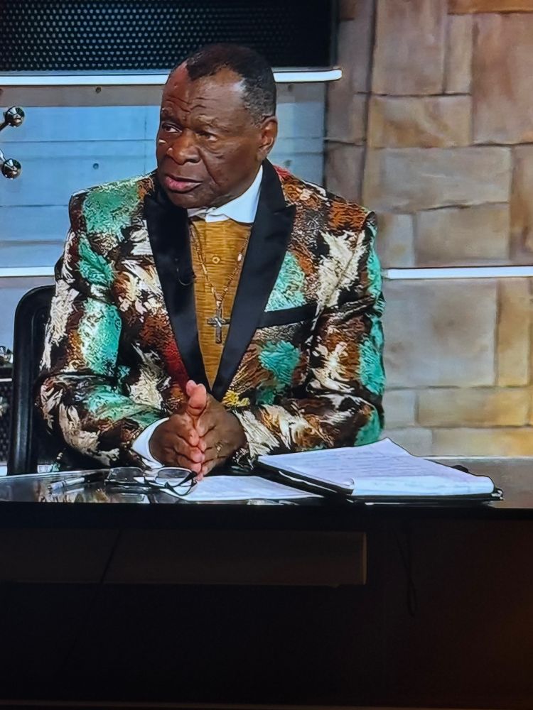 Hall of famer and longtime houston rockets announcer Calvin Murphy in one of his famous loud jackets, this one is brocade in green and brown and white, with a mustard colored sweater and huge cross necklace 