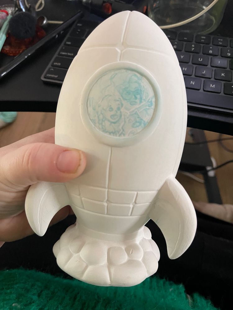 A ceramic rocket meant for crafts but carved to be set with jewels and with a young girl, her aunt, and their most special cat in the porthole of the ship
