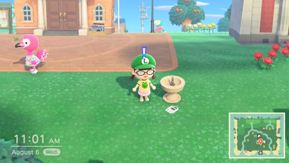 A screenshot of animal crossing new horizons in which there is a transparent custom design of a sega dreamcast vmu near a drinking fountain. 
My player character is wearing oval glasses, the luigi hat, a frog shirt, and a pink tennis skirt.
Flora, the flamingo is in the background near the town hall.