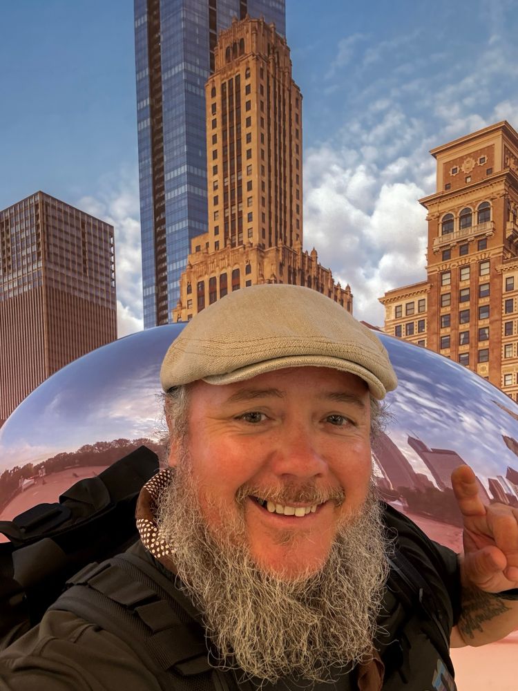 A man in a cap posed in front of a metal bean. 