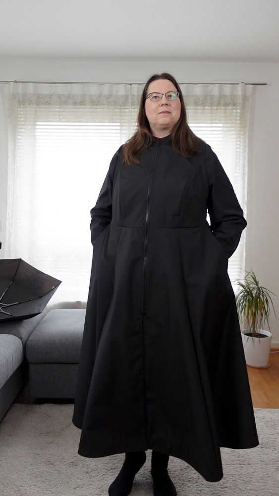 Full body image of a woman in a black raincoat. The hands are in the pockets.