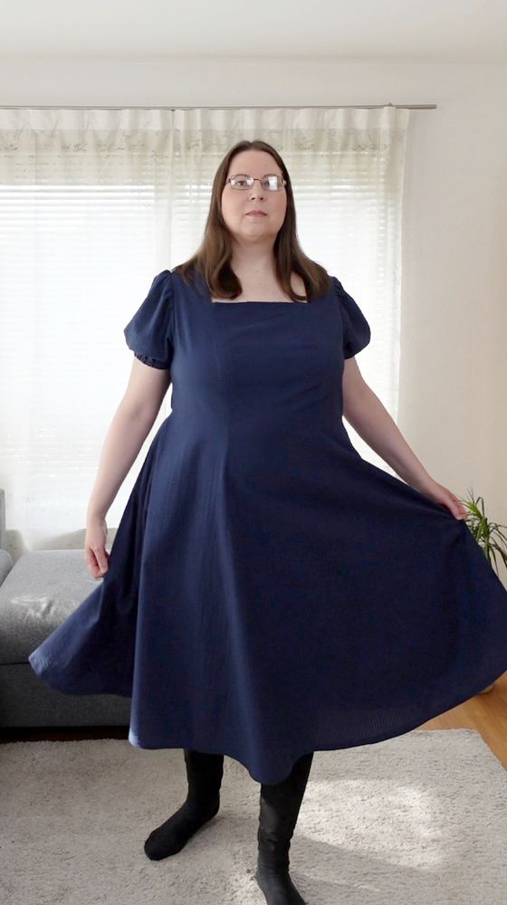 Woman twirling in a blue princess line dress with wide flaired skirt and a square neckline.