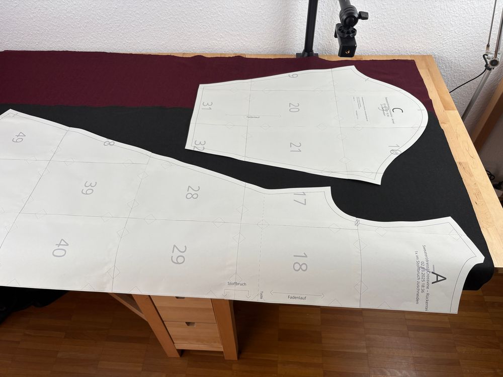 Two pattern pieces, dress back and sleeve spread out on fabric on a table.