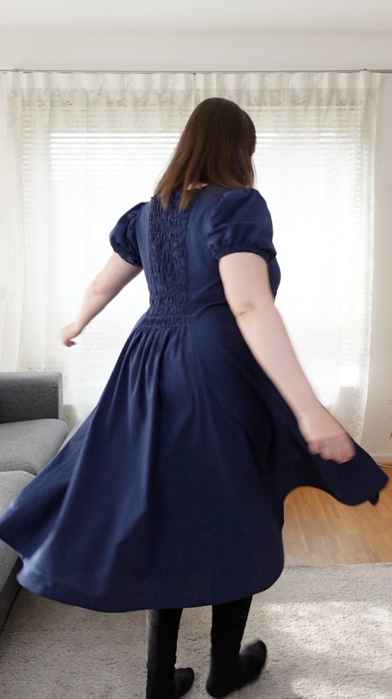 Back view of a woman twirling in a blue dress with shirred back panel