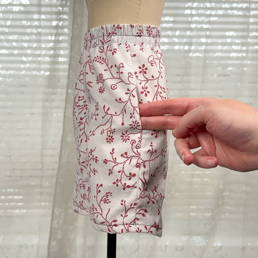 White Boxershorts with red floral pattern on a half scale dressform. A hand is showing where the pockets sit.