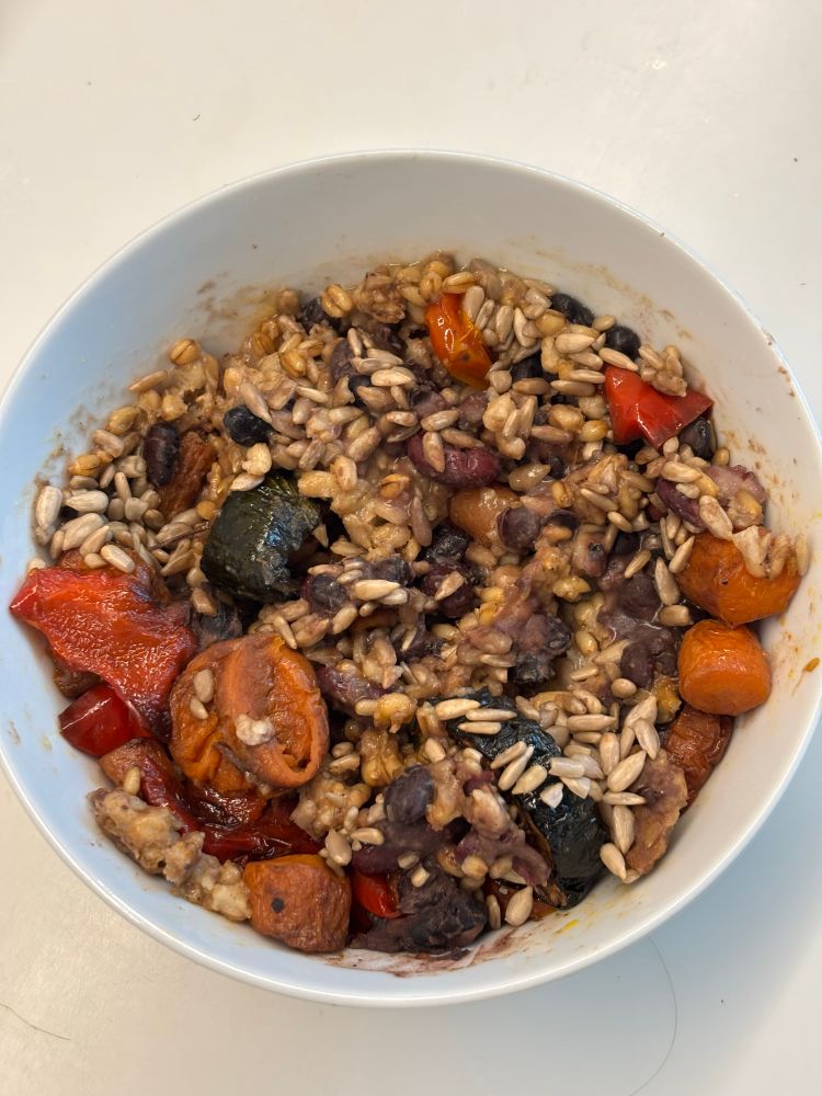 A white bowl filled with oat groat porridge, served with black beans, sunflower seeds and roast vegetables