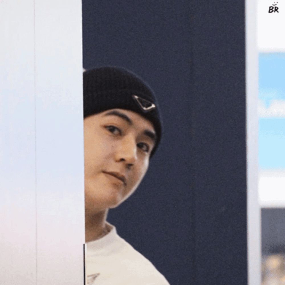 a man wearing a black beanie is peeking out from behind a wall with the letters br above him