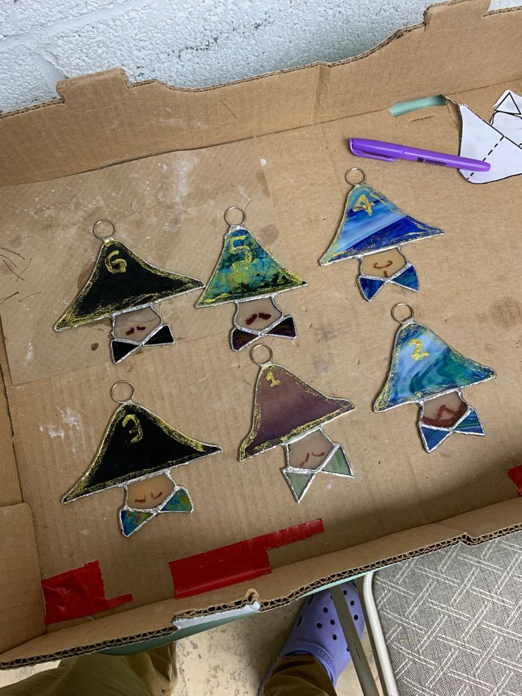 6 stained glass art pieces of the enanos for la bajada de la virgen 2025. Each piece is 4 pieces of glass. The napoleon hat. The face. And 2 pieces for the bow ties. The pieces are numbered 1 - 6