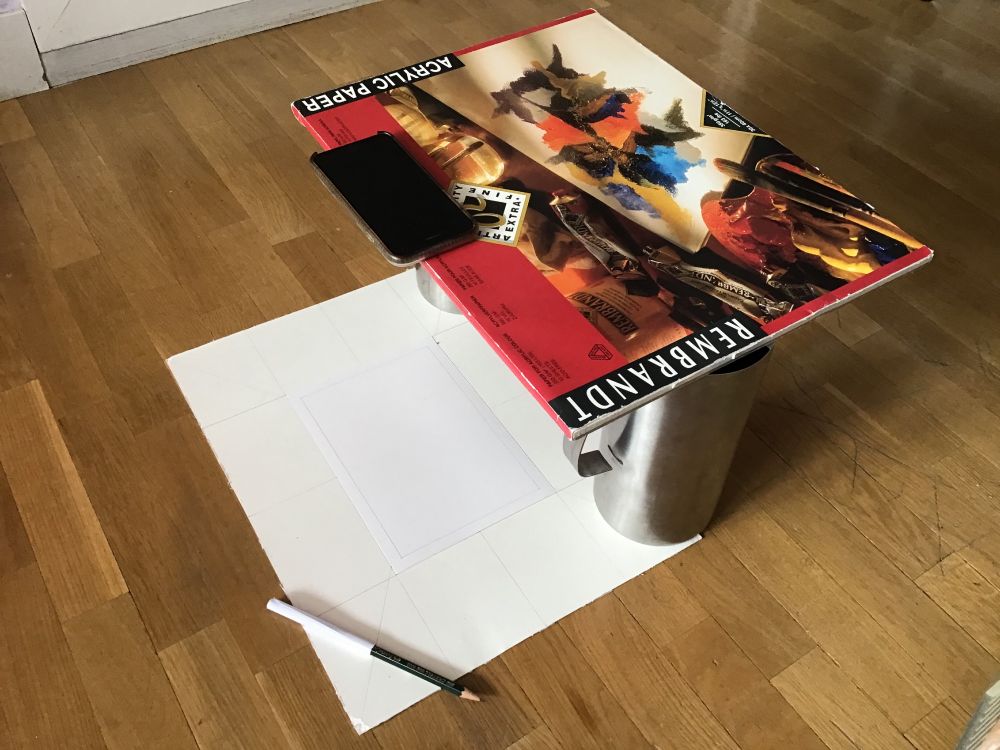 An improvised setup for creating stop motion. A drawing pad balancing on two jugs over a sheet of paper.