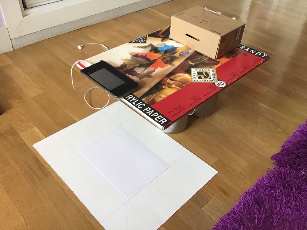 An improvised setup for creating stop motion. A drawing pad balancing on two jugs counterbalanced with a box. Set over a sheet of paper.