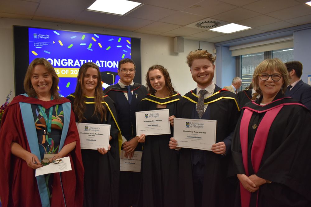 A selection of prize winners stood together in graduation robes with Director of Education Olwyn Byron (left) and Head of School Julia Edgar (right) in the Sir Graeme Davies Building common room.