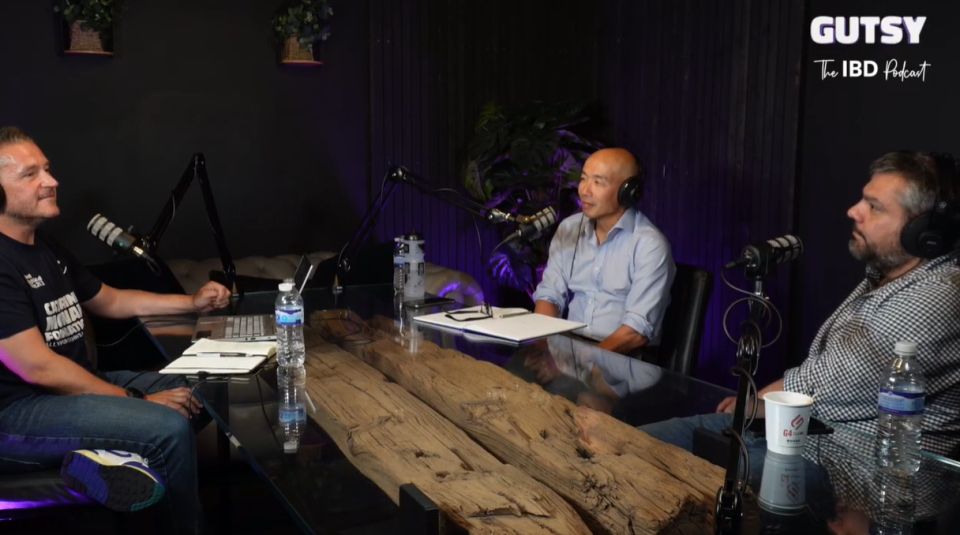 An image of podcast host Derek McEwan and experts Gwo-tzer Ho and Konstantinos Gerasimidis sat in the studio with mics and a large wooden desk. Derek is sat to the left, with Gwo-tzer and Kostas on the right, facing Derek.