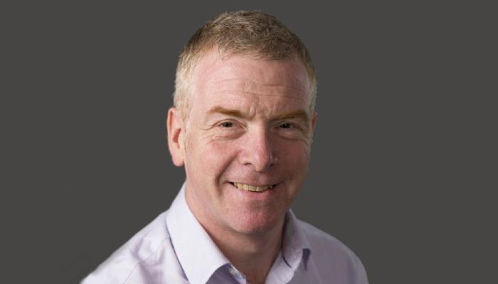 A portrait image of Simon Milling, with his head and shoulders visible against a dark grey background.
