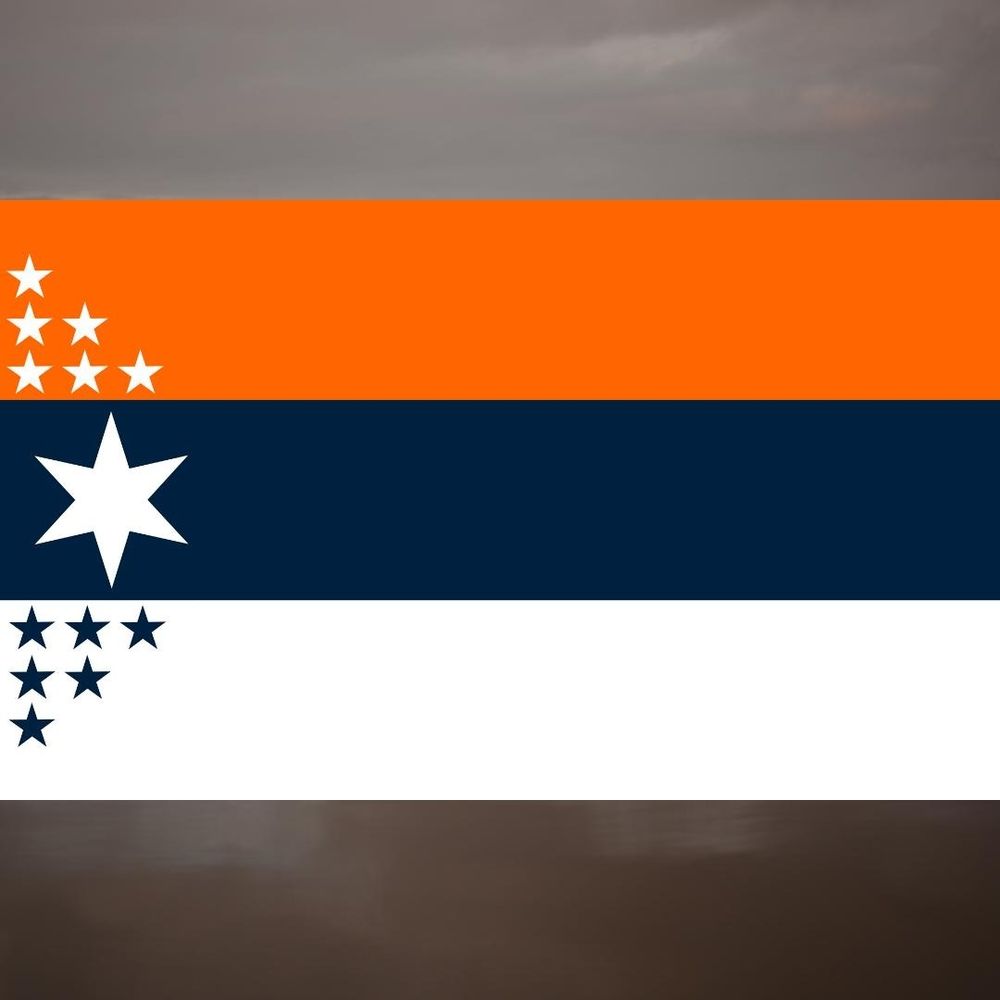 A flag consisting of three horizontal bands: a red-orange top band, a navy blue middle band, and a white bottom band.

In the upper left corner of the flag, there are six white, five-pointed stars arranged in a triangular pattern.  In the center, slightly to the left, is a large, eight-pointed white star. In the lower left corner, there are six dark navy blue, five-pointed stars, also arranged in a triangular pattern.

The background is a blurry gradient of dark grays, suggesting a stormy or overcast sky.