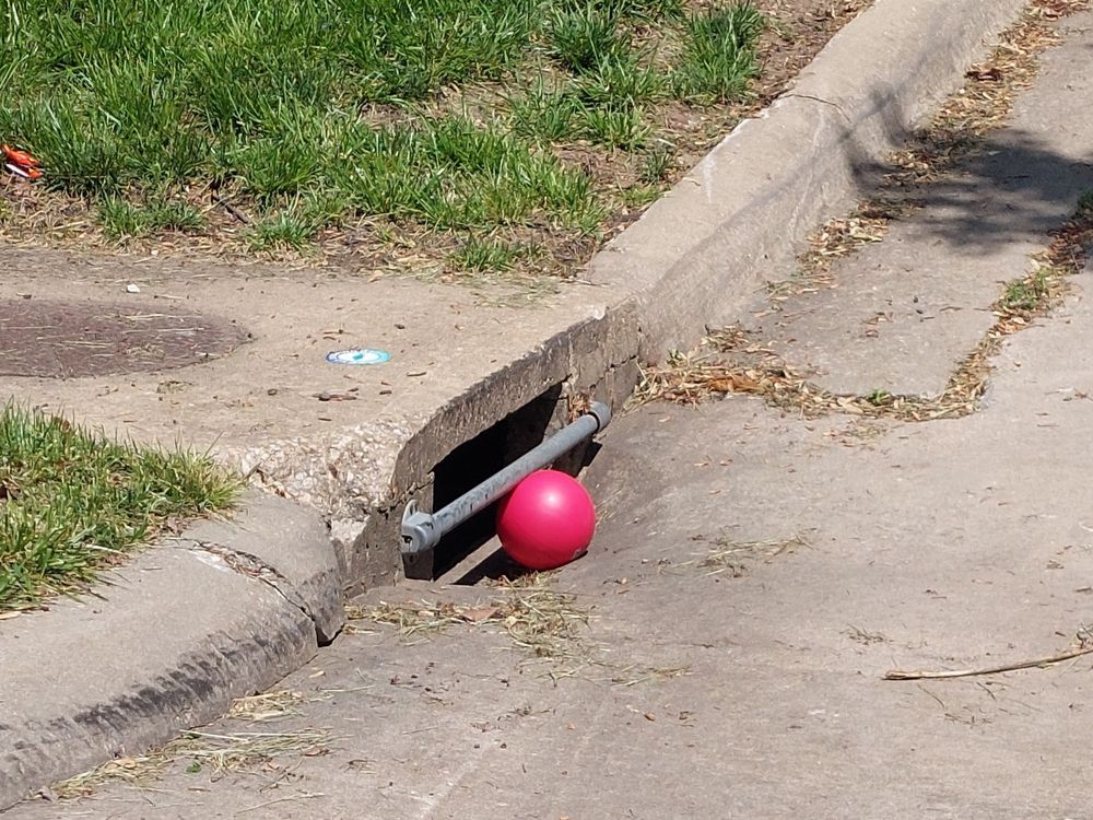 A red ball sits in front of a storm drain