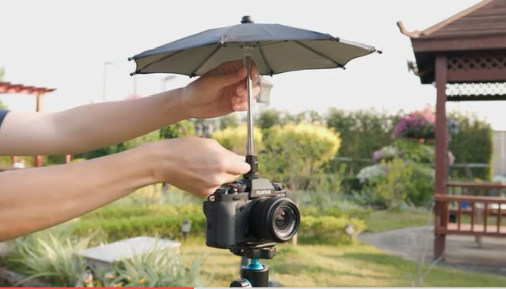 Person attaching a small umbrella to a digital camera's cold shoe attachment. 