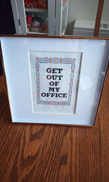 A cross-stitch pattern reading "get out of my office" in a frame.