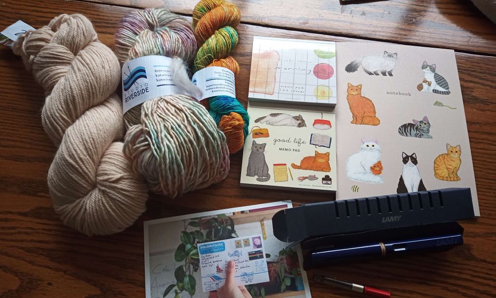 Three skeins of yarn and various cute stationary on top of a table.