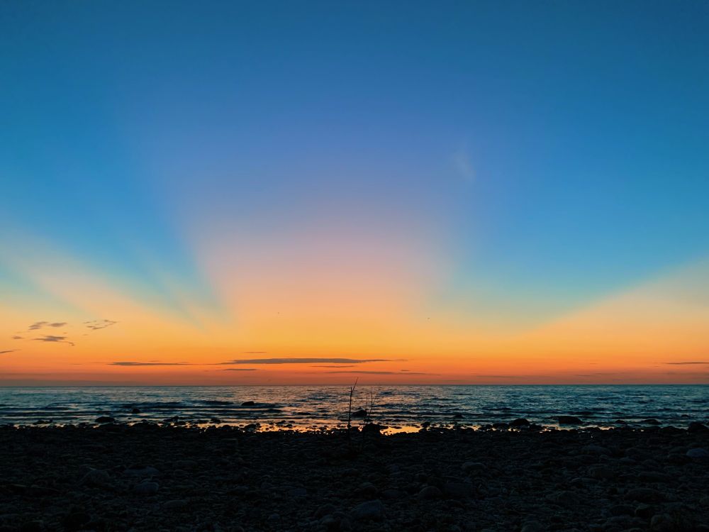 Looking out across the water, a glowing orange sunset at the horizon against a rich blue sky 