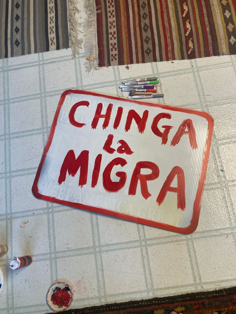 Chinga La Migra painted in red, on a sign with a white background. The white has been painted over a yard sign for the orange turd's 2020 presidential campaign. That sign was stuck in my lawn, and I am repurposing it