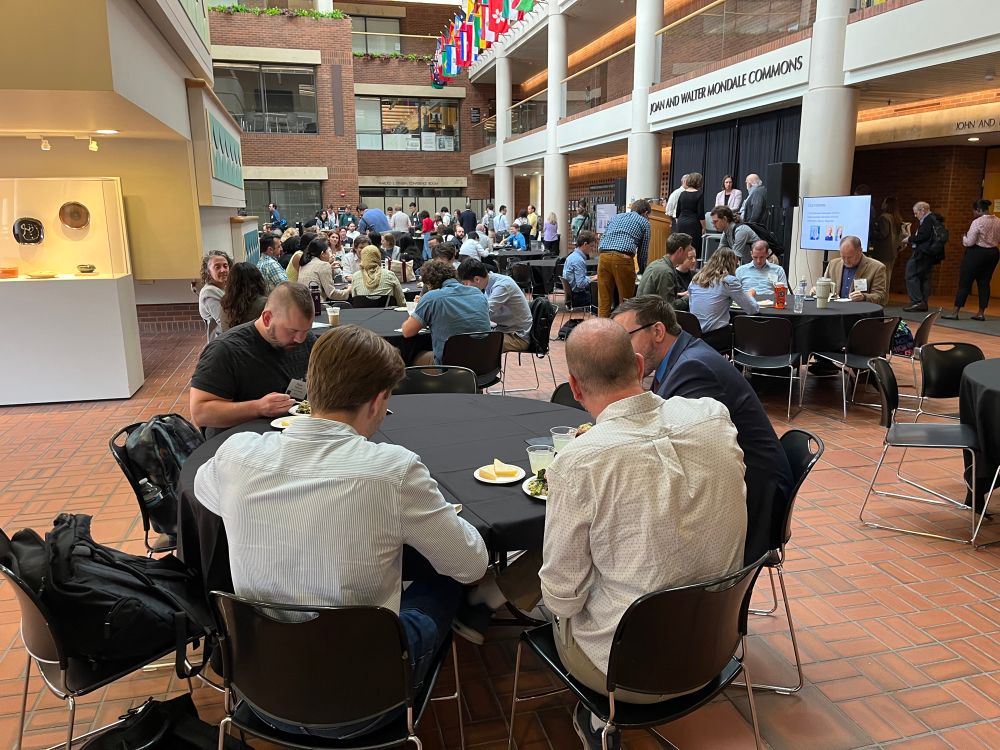 People sit around tables eating lunch and listening to a keynote presentation 