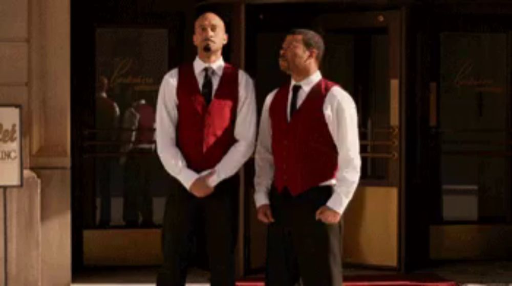 two men in red vests stand in front of a sign that says hotel