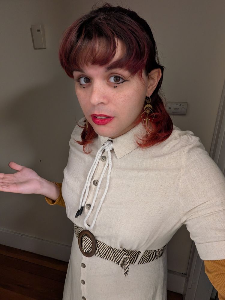 Temperance straight up looks like a doll. It has bright red lips. It's wearing a white collared dress with a zebra pattern and dangly brass earring with swords, moons, and stars. It has a rope tied around its collar with a sheet bend knot. It looks exceptionally pale in this lighting (and temperature) and is making a bit of a "what gives?" gesture. 