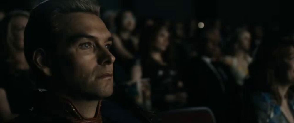 a man in a suit is sitting in a dark room with a crowd behind him .