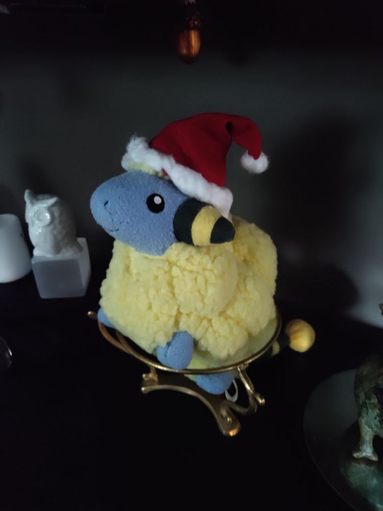 A plushie of the Pokemon mareep wearing a cute little santa hat