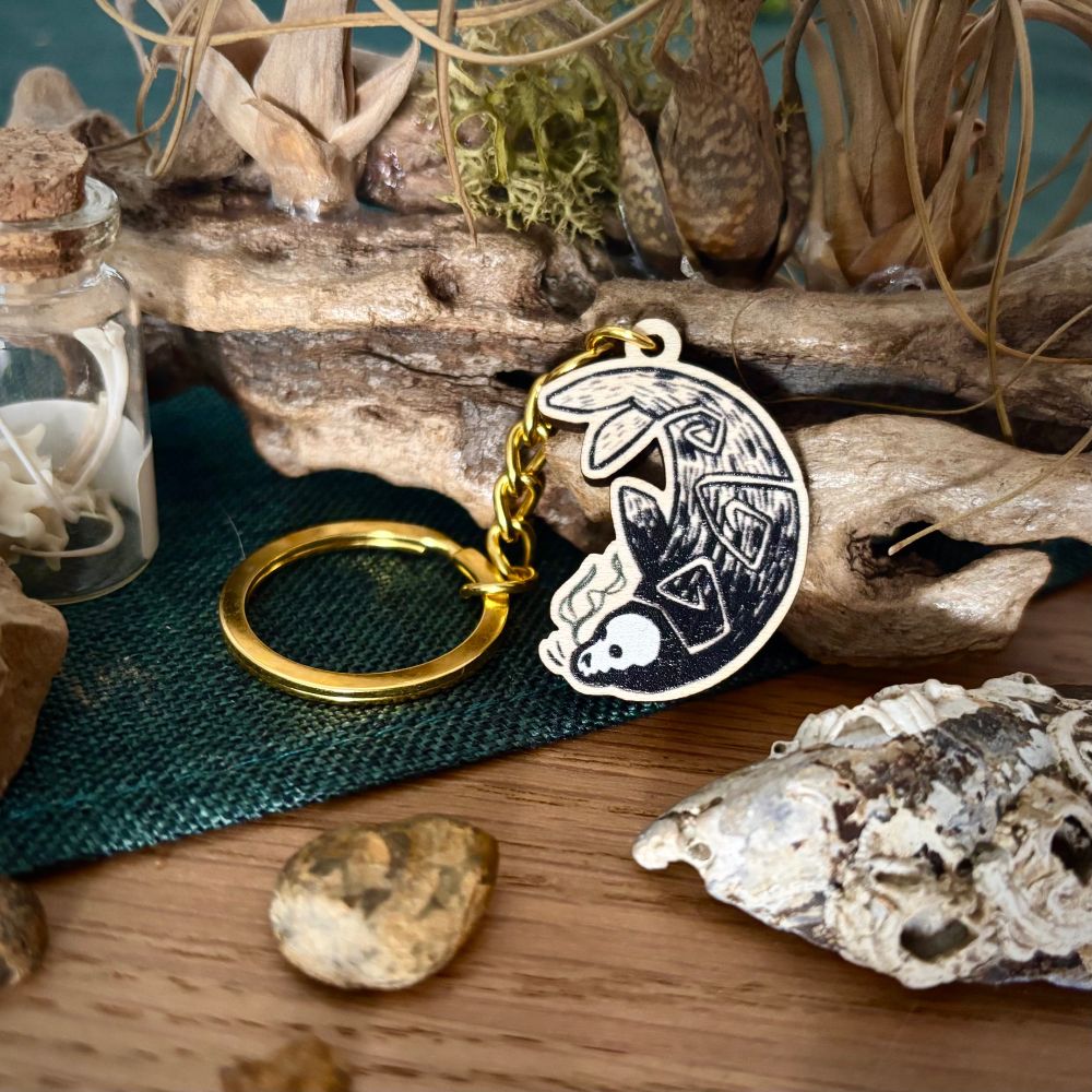 Wooden keychain of a seal with a skull in place of its head, its body decorated with spirals 