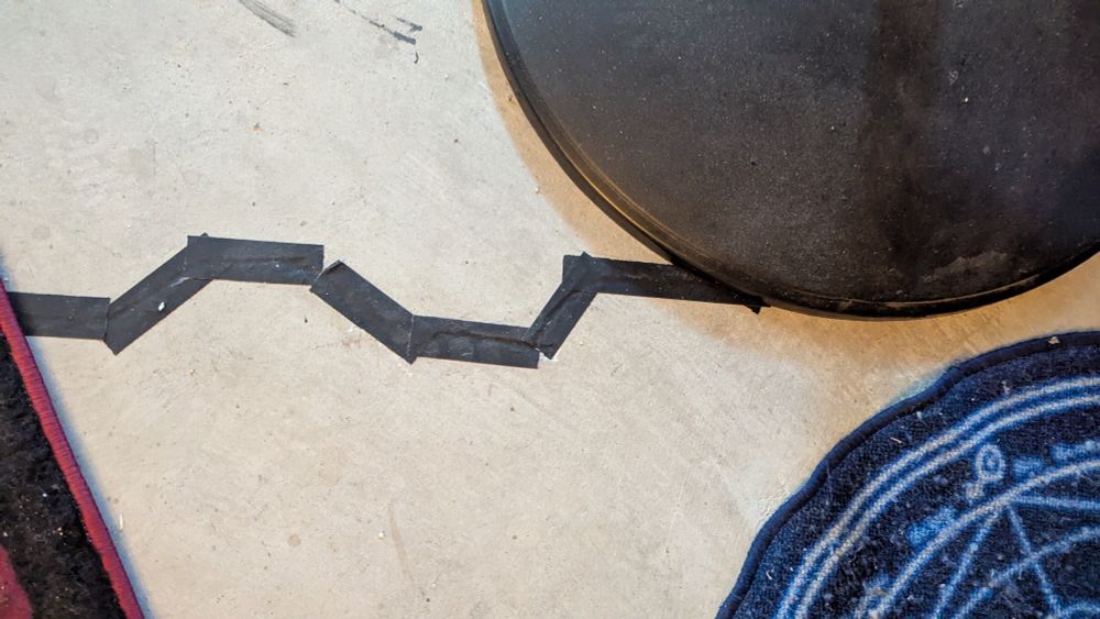 A photo of a concrete foundation with a jagged line of black tape covering a long, thin crack.