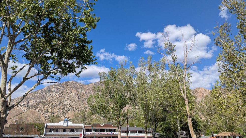 An image of the sierra mountain landscape with a bright blue sky and the rooftops of a few Old-West looking buildings.