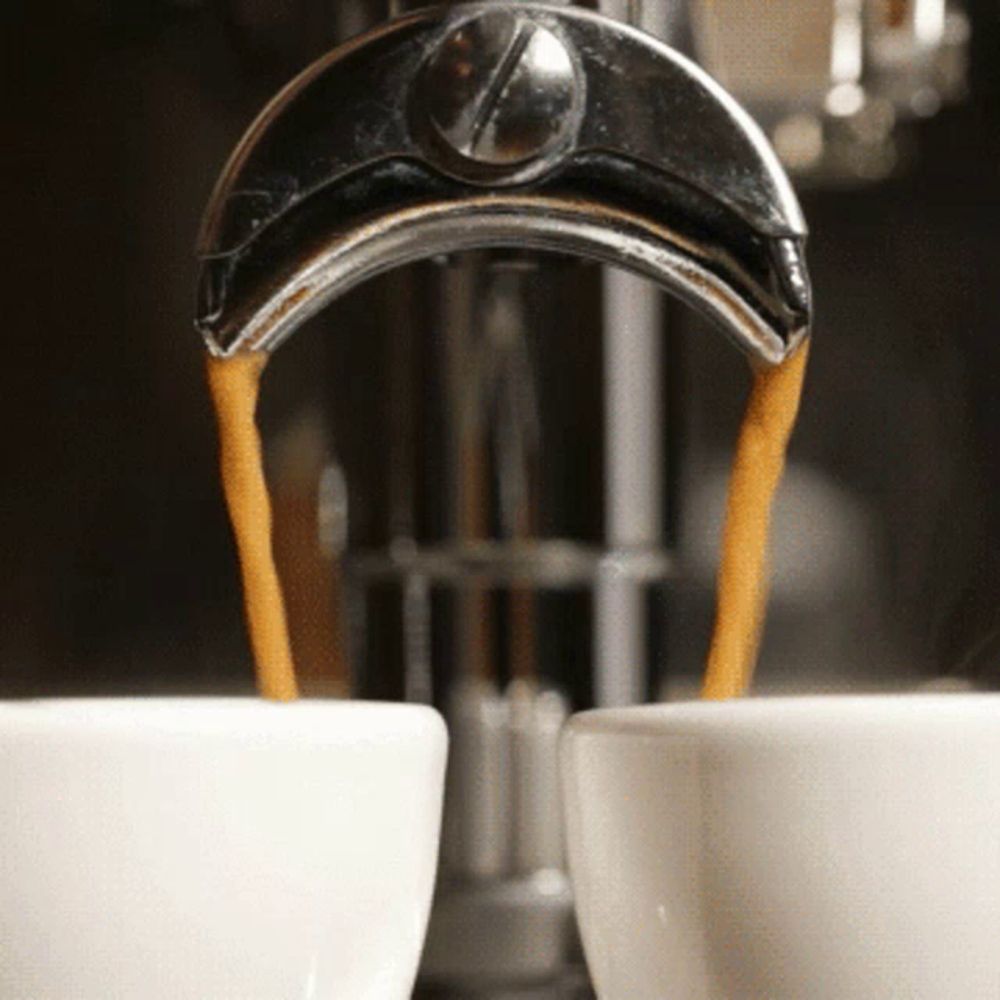 two cups of coffee are being poured from a coffee maker