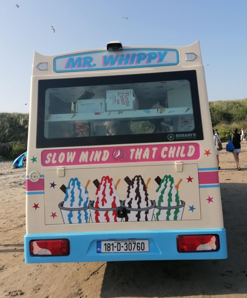 Back of an ice-cream van on the beach it has a long thin sign halfway down that say "slow mind (volkswagon logo) that child"