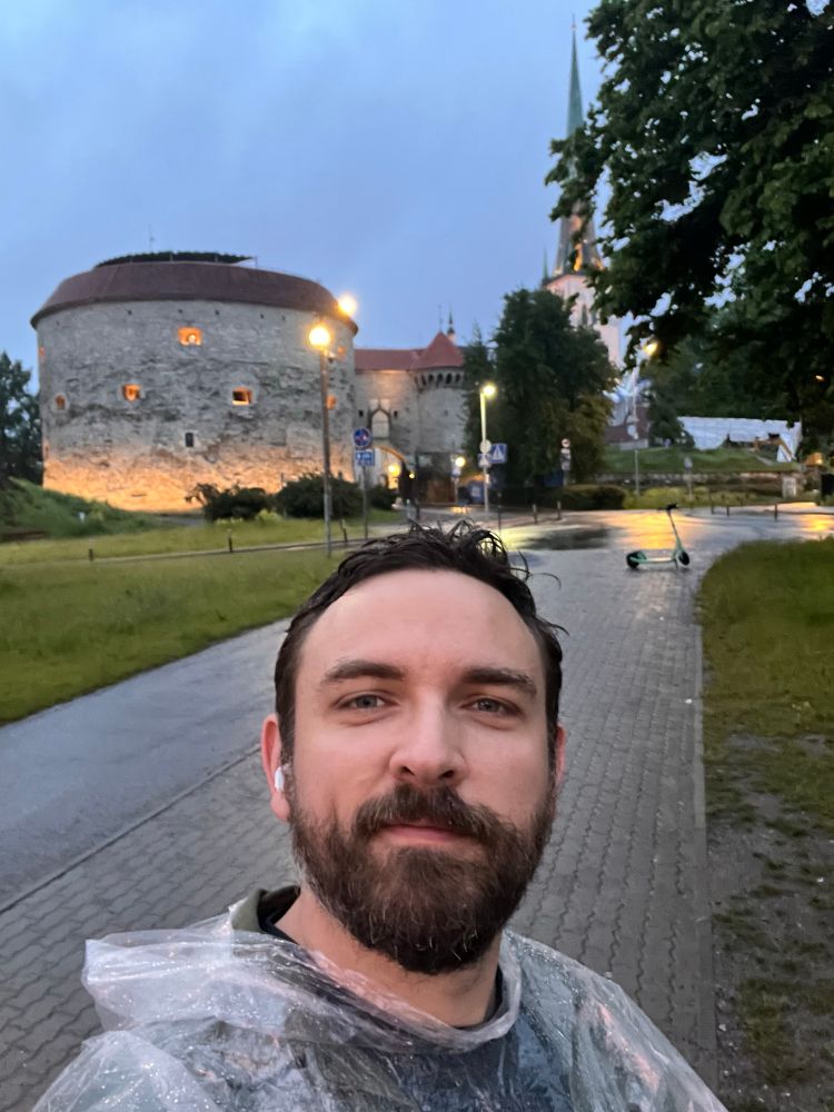 A bearded man wearing a rain coat takes a picture in front of Tallinn Old Town