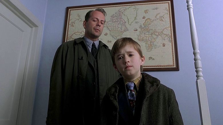 Malcolm (Bruce Willis) and Cole (Haley Joel Osment) stand in a bedroom looking downward at the camera in The Sixth Sense (1999).