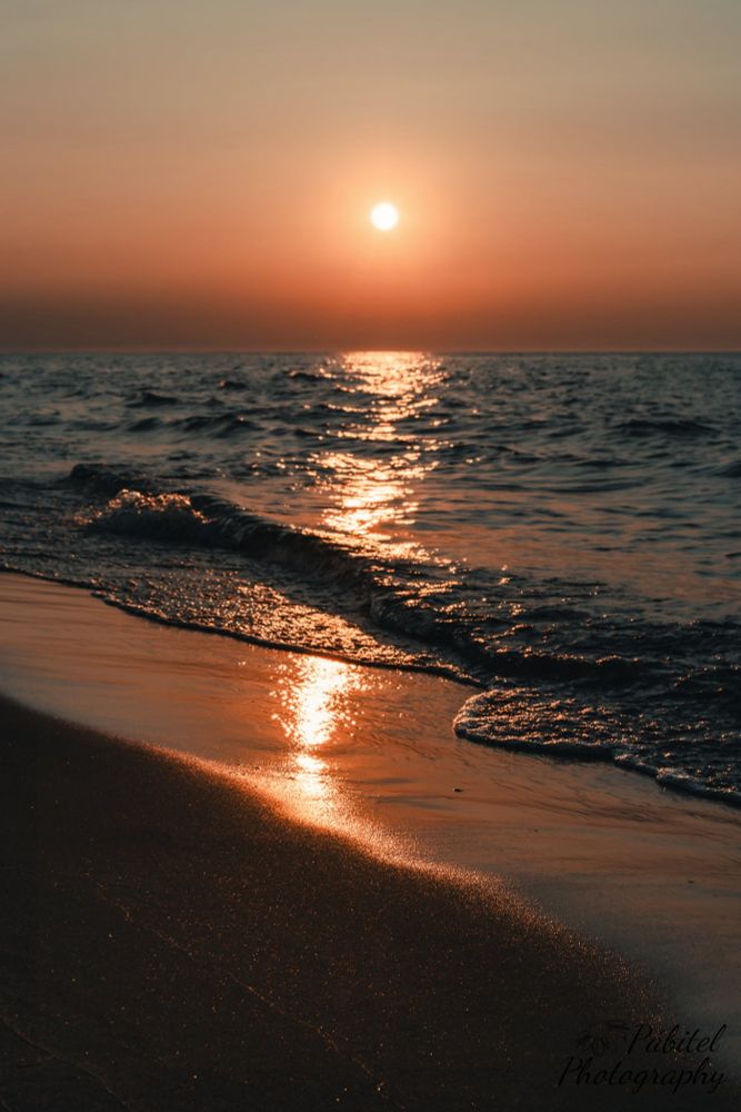 Low angle view of a sunset over a lake with sand that is sparkling. 